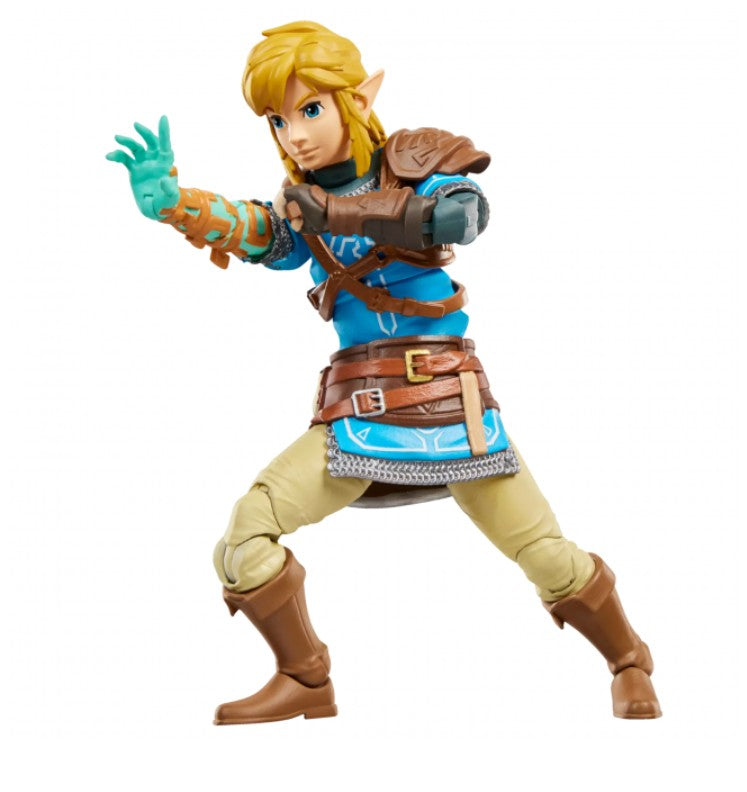 A Link action figure posed in a dynamic combat stance, featuring blonde hair, a blue tunic, brown leather armor, beige trousers, and green gloves, set against a plain white background.